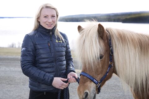 Sara står brevid en islandshäst i grimma med Alsensjön i bakgrunden