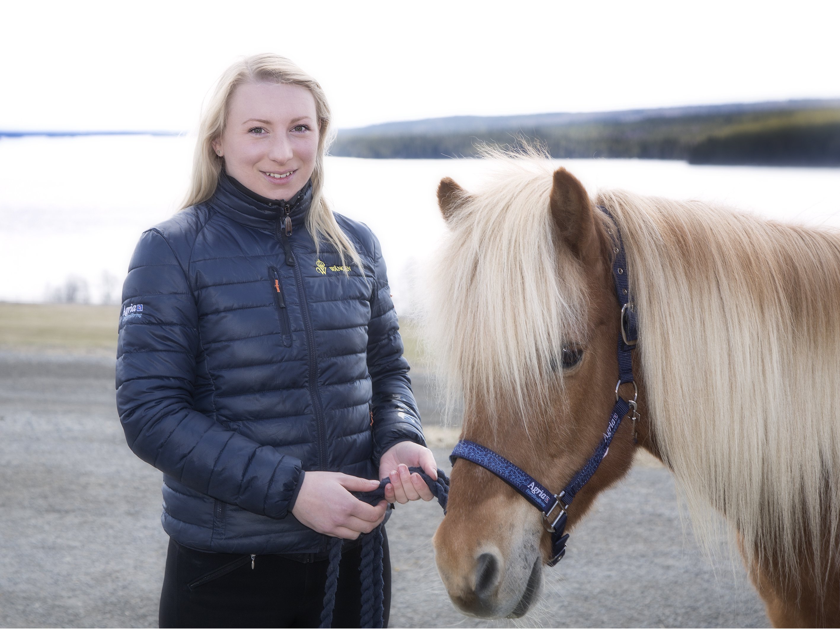 Sara står brevid en islandshäst i grimma med Alsensjön i bakgrunden