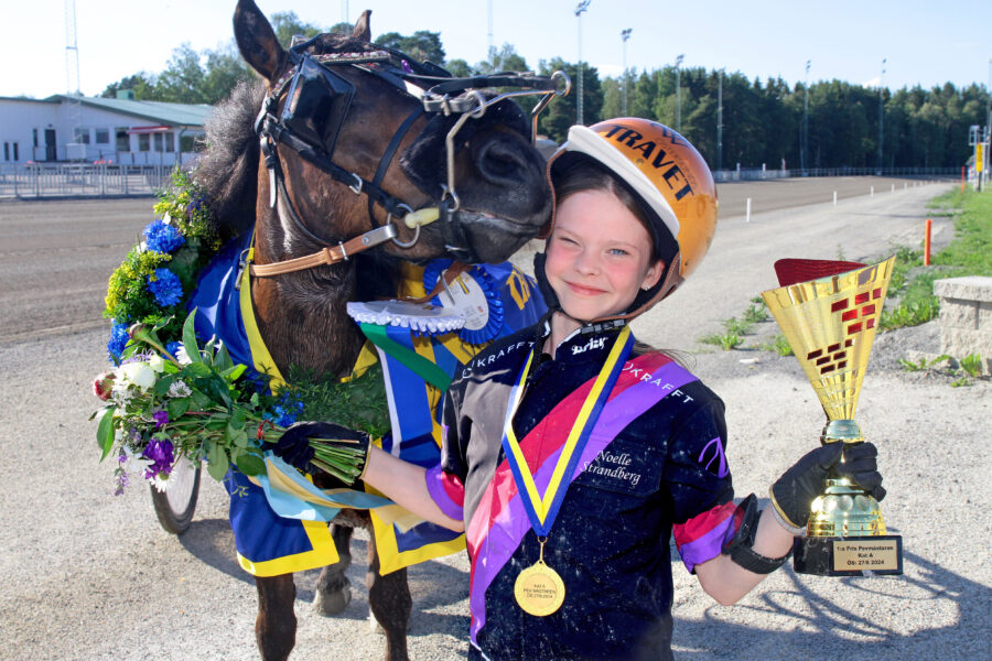 En ponnykusk firar en seger. Kusken har en trofé och bär en medalj. Hästen pryds av en blomkrans och ett blågult täcke.