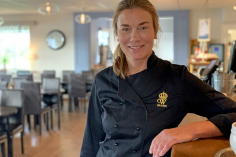 Annika Gripenberg står i restaurangens matsal, i svart serveringsjacka med Wångens gula emblem på.