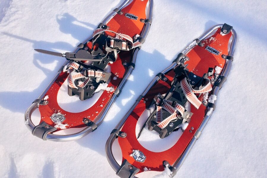 Ett par röda snöskor med metallramar och remmar ligger på snön och inbjuder till vinteraktiviteter och oförglömliga upplevelser.